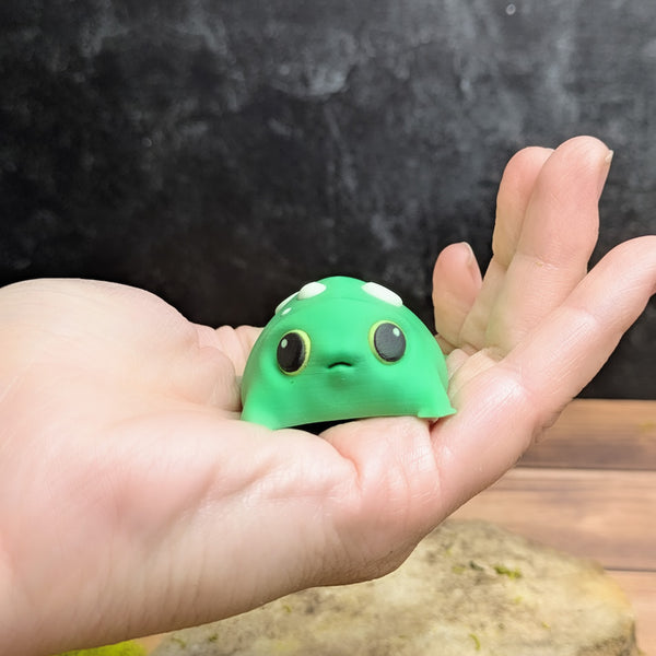 Blob frog sitting in the center of an open palm, emphasizing its small, plump size and slightly startled expression.