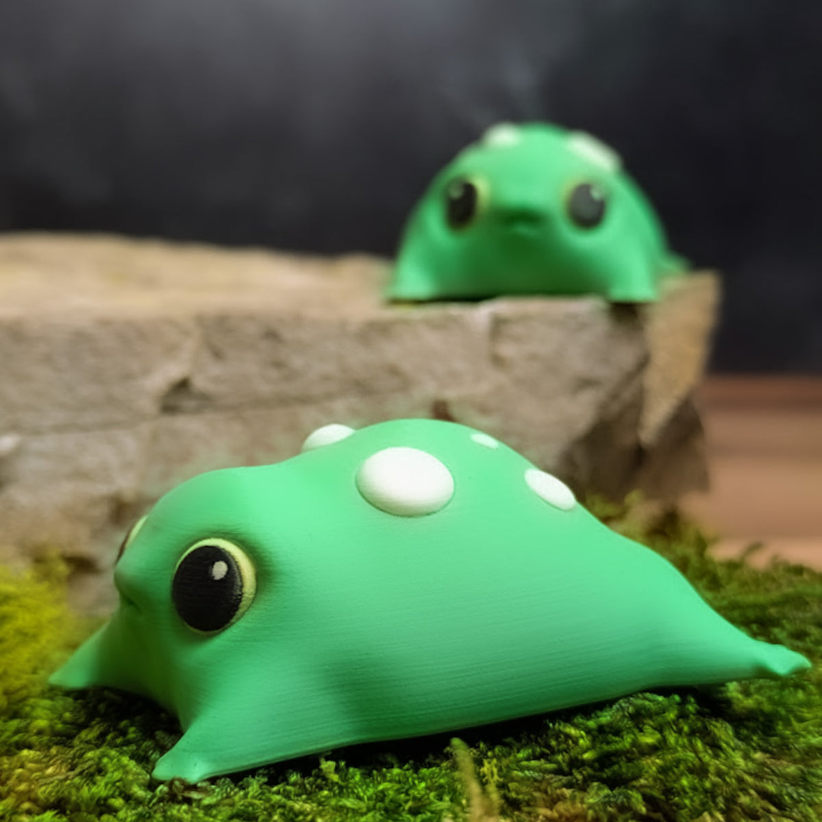 Side profile of the blob frog resting on moss, showing the rounded shape, white spots, and subtle foot nubs.