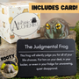 Judgmental frog toy with packaging and description card on a grassy background