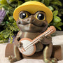 Close-up of a frog figurine with oversized eyes, yellow sun hat, and a banjo resting in its hands.