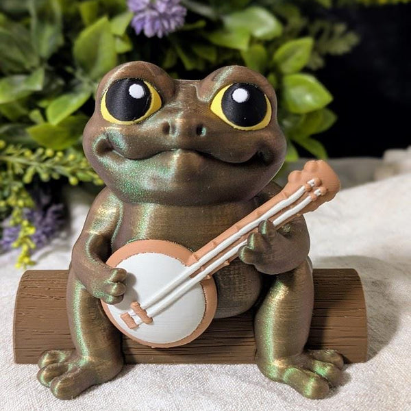Frog figurine with a banjo and yellow hat sitting on a surface, surrounded by purple flowers, without a hat