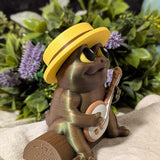 Side view of a frog figurine in a yellow hat, mid-banjo serenade, surrounded by leafy plants and flowers.