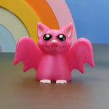 Pink 3D printed bat figurine with big eyes and wings, pastel goth desk buddy