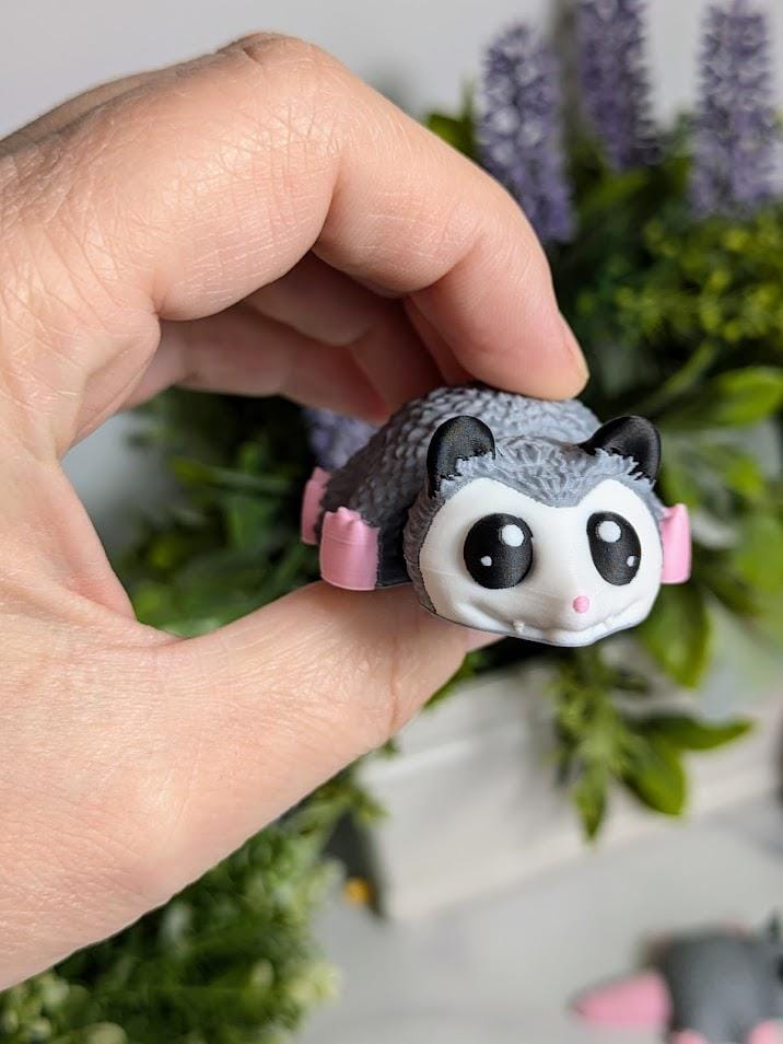 A close-up of a hand pinching the Blob Possum's squishy middle, emphasizing its small size and soft expression.