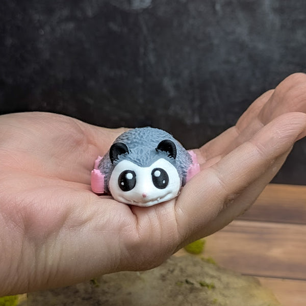 The blob possum figurine resting in a human hand, showing its small size and rounded shape.