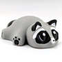 A small, fat raccoon with adorable eyes sits on a white background.
