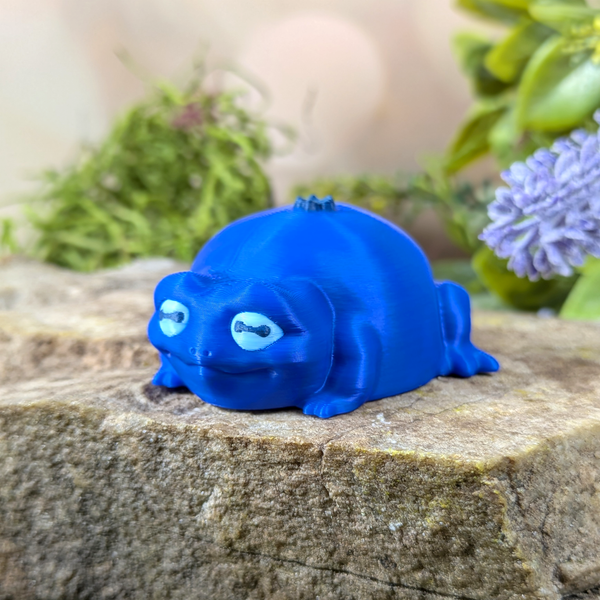 Blueberry Frog figurine sitting on a rock, angled view showing its soft features and sculpted blueberry stem.