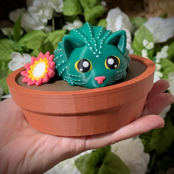 Green cactus cat figurine with flower, sitting in terracotta pot with wide-eyed expression.