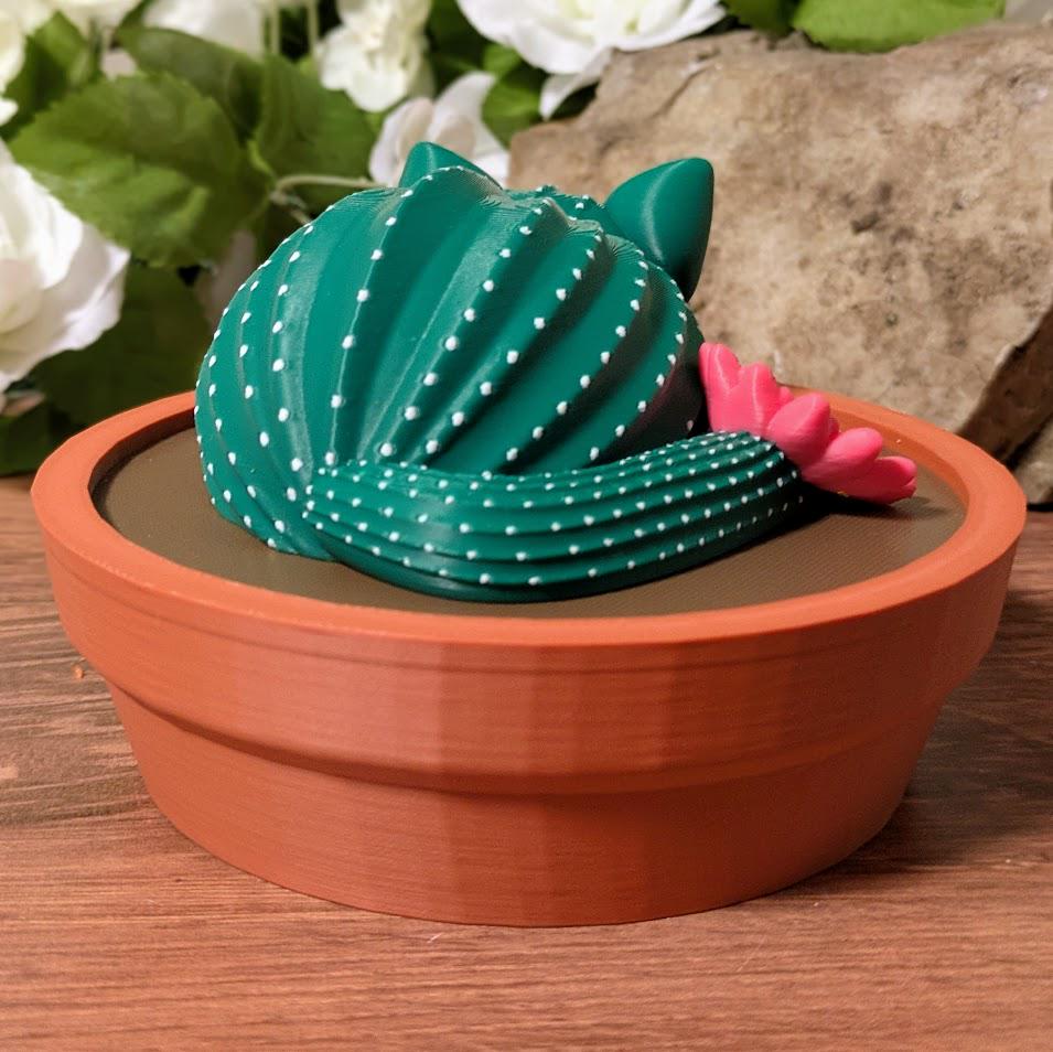 Cactus cat figurine in pot viewed from behind, pink flower peeking out.