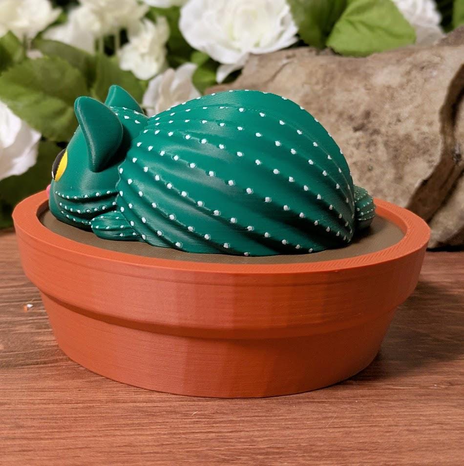 Side view of cactus cat curled in terracotta dish, textured like a cactus with dotted ridges.