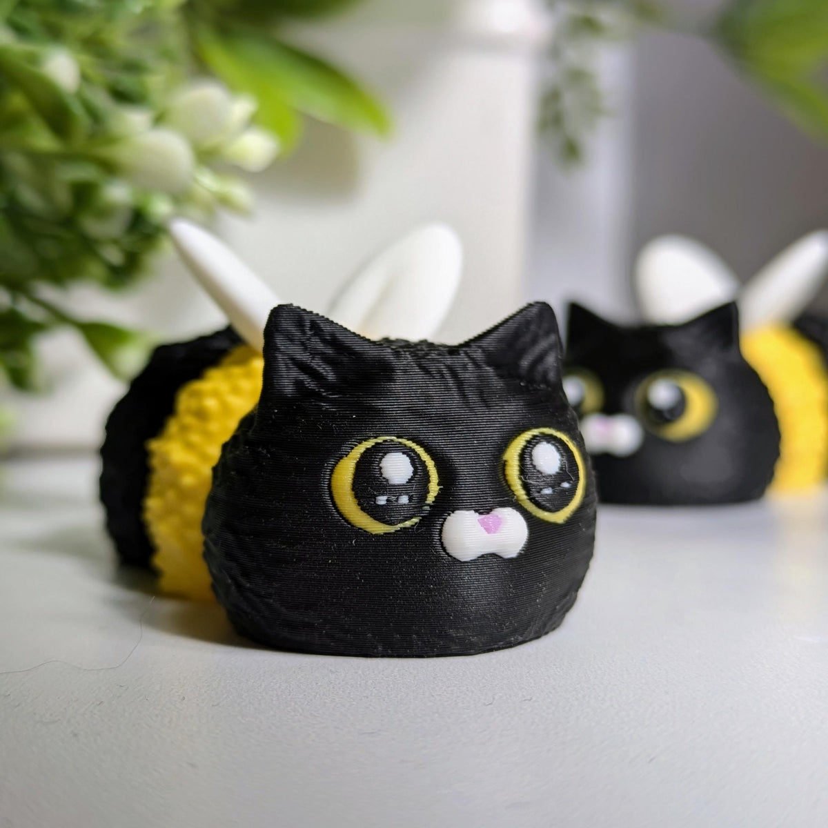 Close-up of the Cat Bee’s wide yellow eyes and perky ears, with another bee-cat buddy blurred in the background.