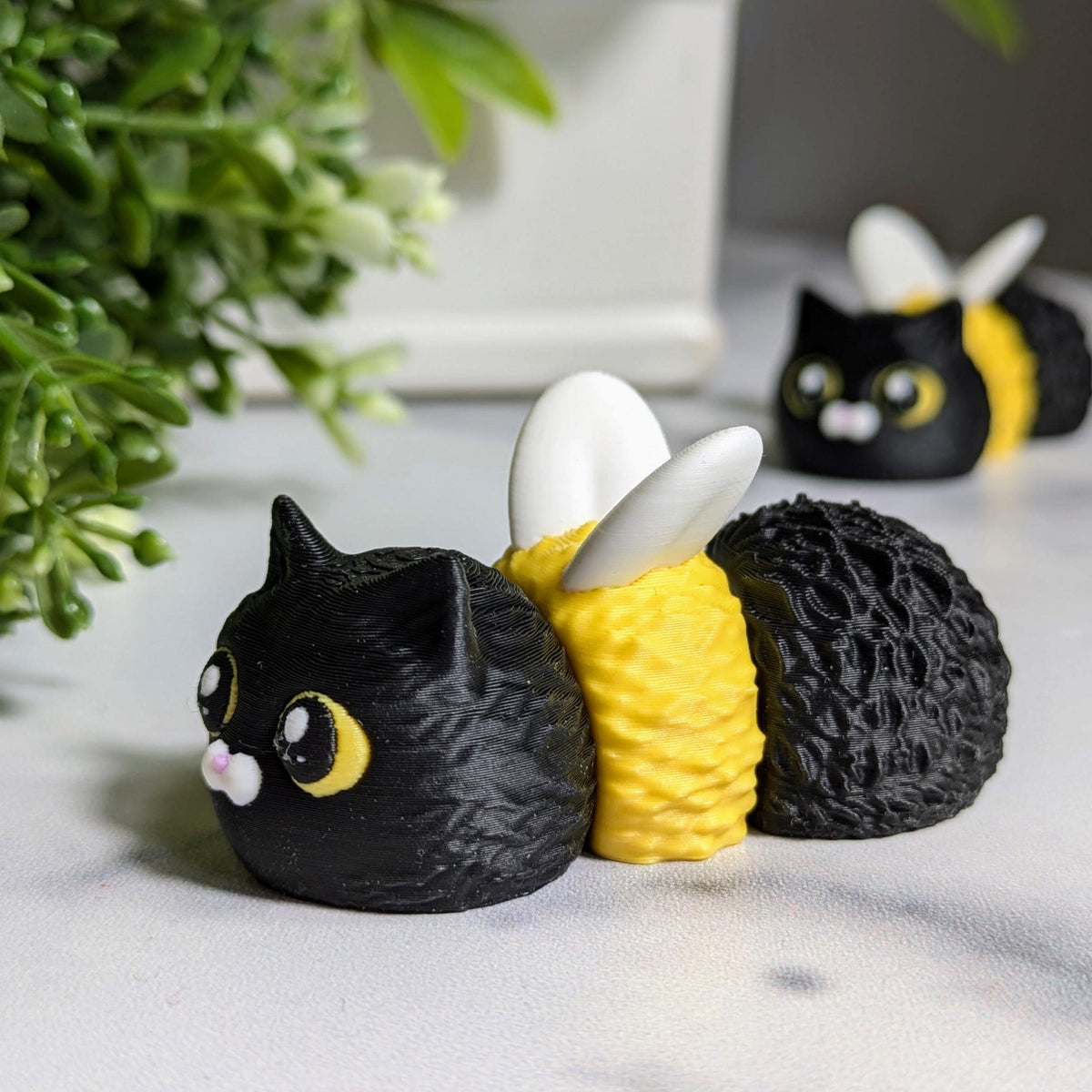 Cat Bee faces forward in a leafy setup, flaunting its round yellow body, perky ears, and bee wings.