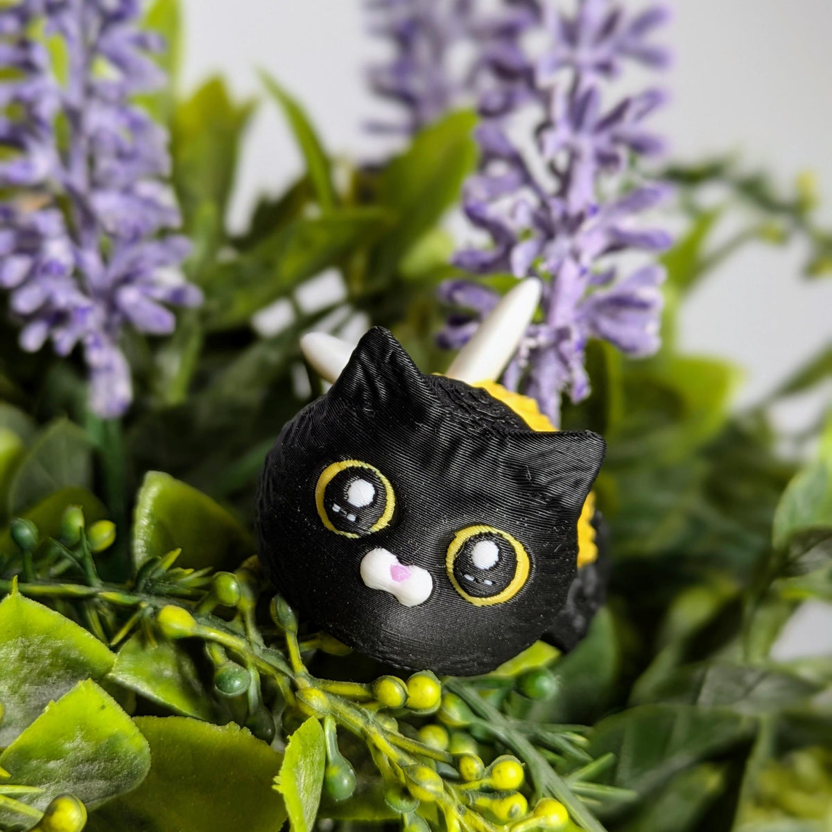 Cat Bee rests among purple flowers with wide, mischievous eyes and a floral garden vibe.