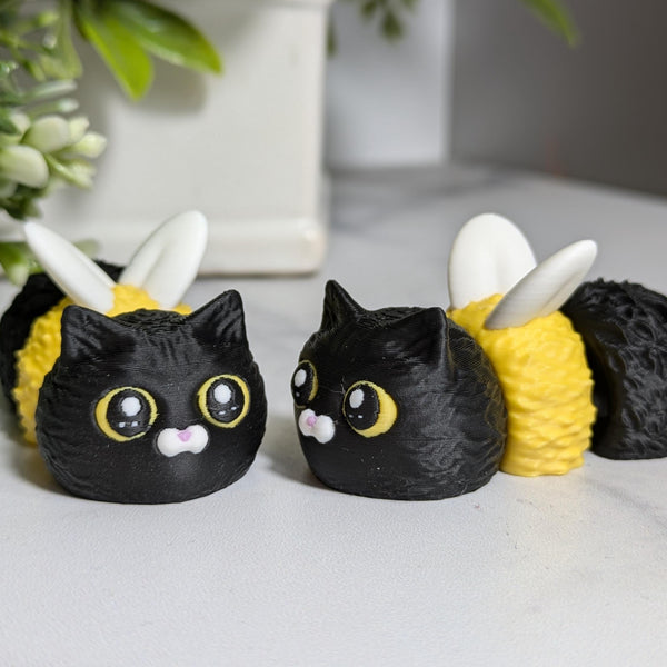 Two Cat Bees sit side by side, one facing forward and the other glancing to the side like they’re plotting something sweet and fuzzy.