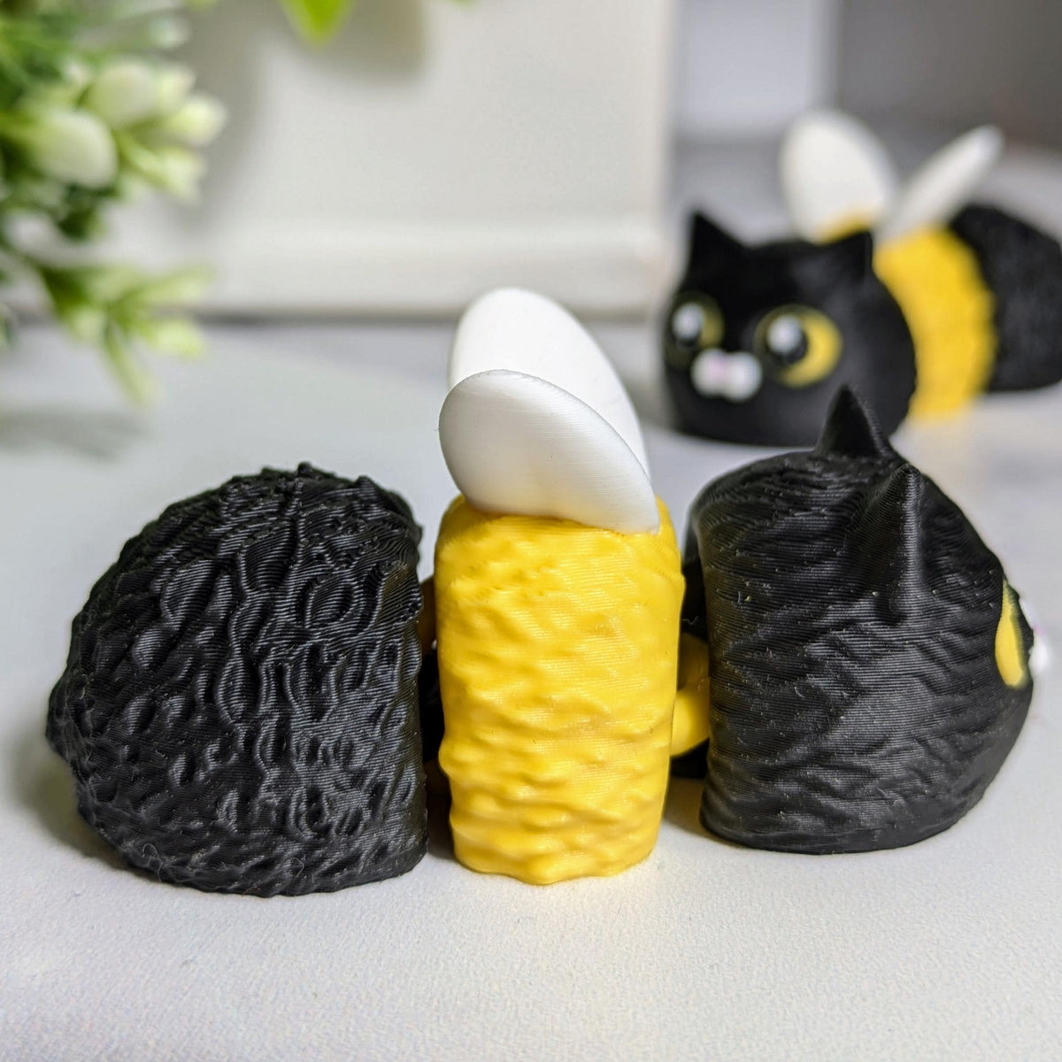 Side view of the cat bee, lying on a white surface with another cat bee in the background.