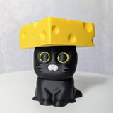 Black cat figurine sporting a yellow cheese wedge hat with circular holes.