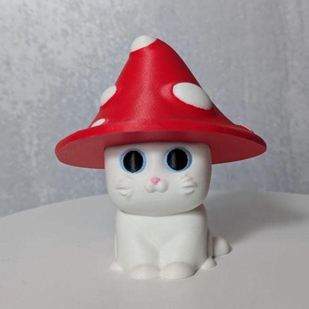 White cat figurine with a red mushroom cap hat featuring white spots.