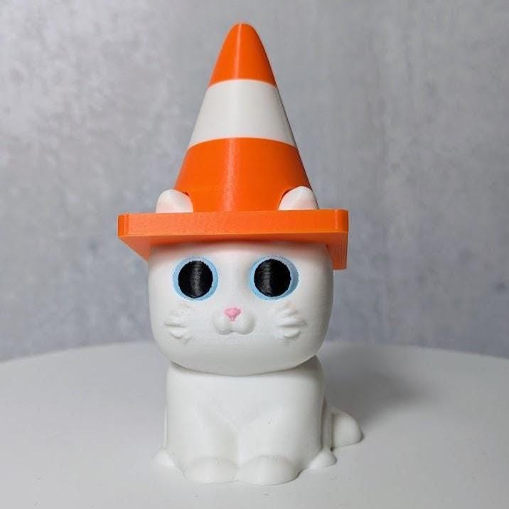 White cat figurine wearing an orange and white traffic cone hat.