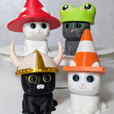 Group of three cat figurines each wearing different hats: mushroom, frog, and traffic cone.