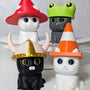 Group of three cat figurines each wearing different hats: mushroom, frog, and traffic cone.