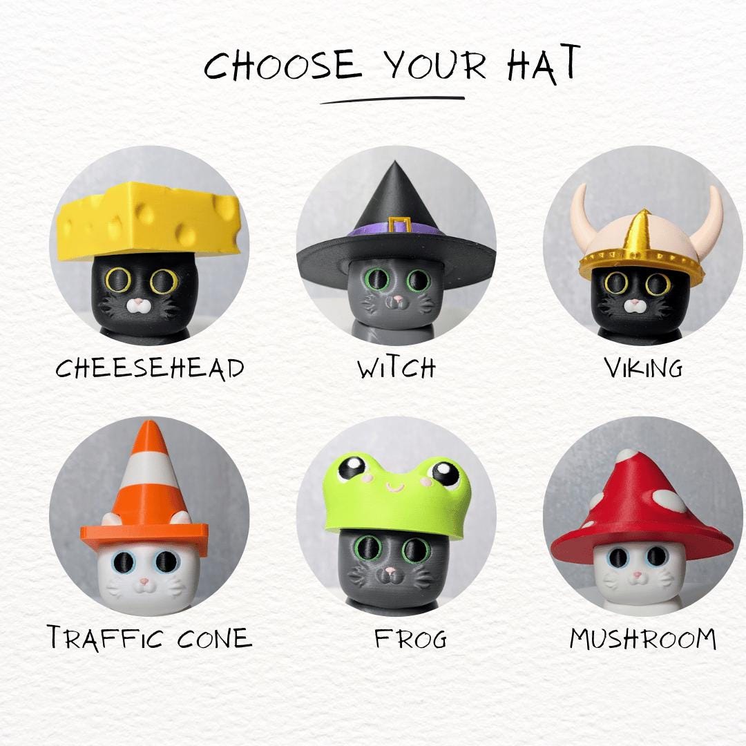 Illustrated display of six interchangeable hats for cat figurines, including cheese, traffic cone, frog, witch, mushroom, and viking styles.