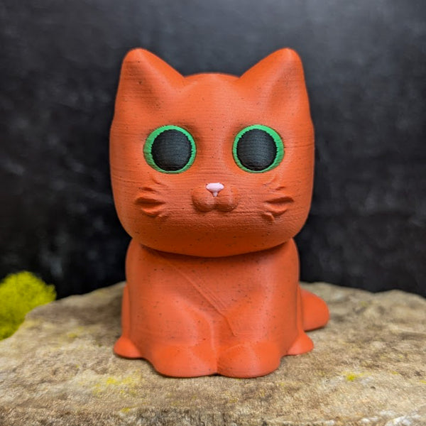 An orange cat figurine with wide green eyes and no hat, showing its small pointed ears and smooth round head.