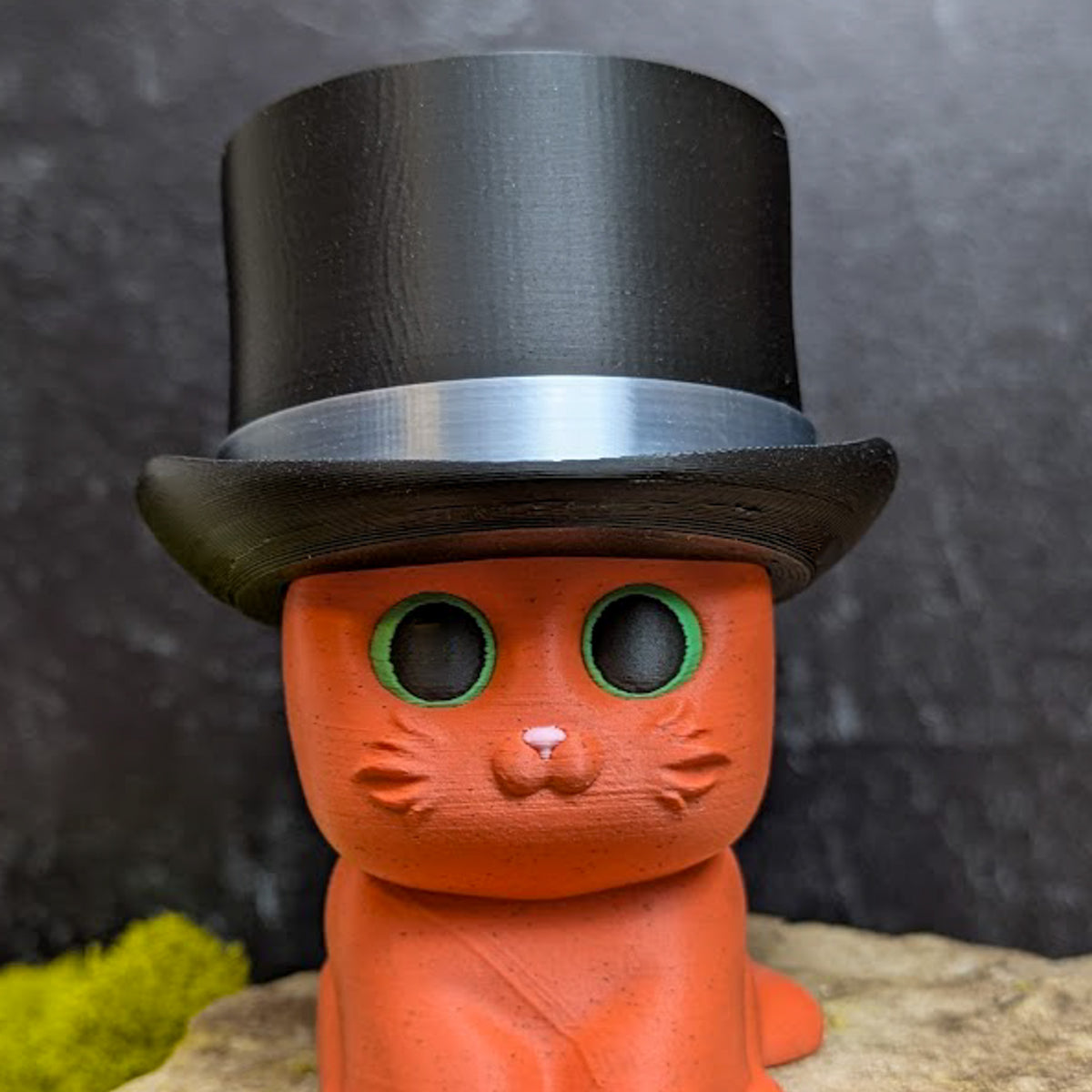 An orange cat figurine wearing a tall black top hat with a shiny silver band.