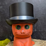 An orange cat figurine wearing a tall black top hat with a shiny silver band.
