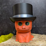 An orange cat figurine wearing a tall black top hat with a shiny silver band.