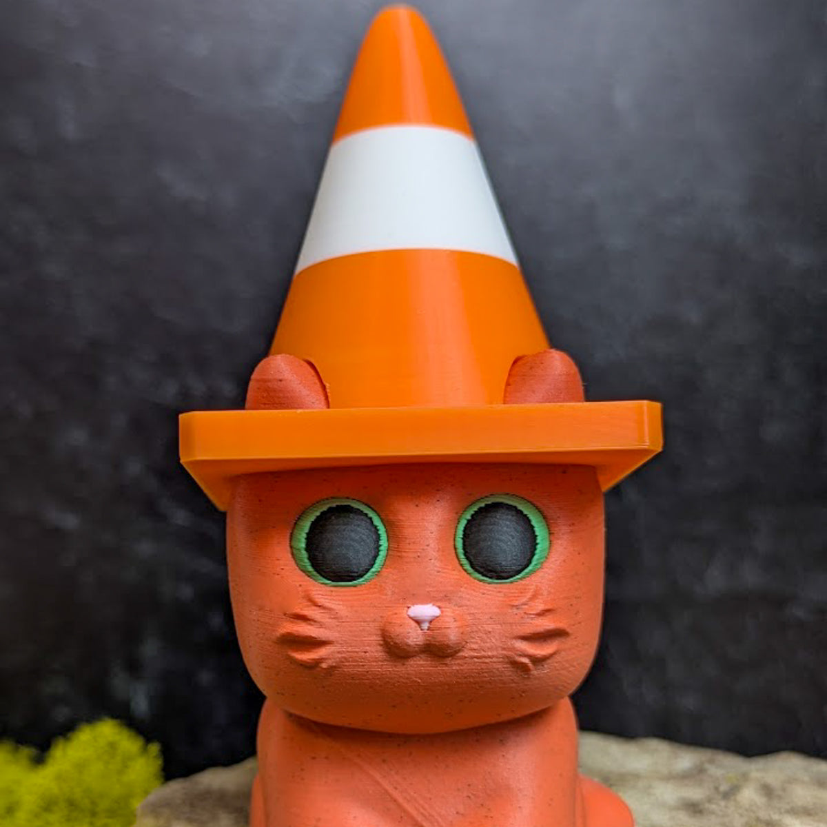 An orange cat figurine wearing a miniature orange and white traffic cone as a hat.