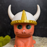 An orange cat figurine wearing a white and gold viking helmet with large curved horns.