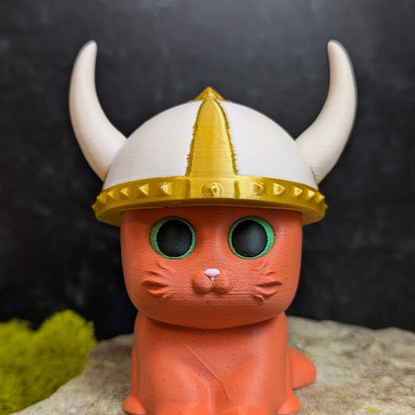 An orange cat figurine wearing a white and gold viking helmet with large curved horns.