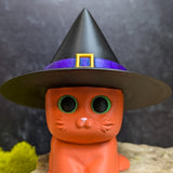 An orange cat figurine wearing a tall black witch hat with a purple band and gold buckle.