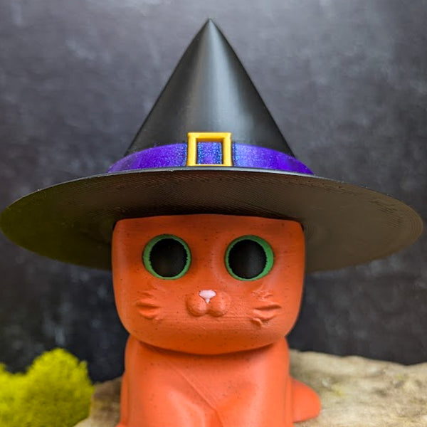 An orange cat figurine wearing a tall black witch hat with a purple band and gold buckle.
