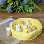 Chicken and egg tic tac toe set arranged inside a nest-style board, surrounded by greenery and flowers.