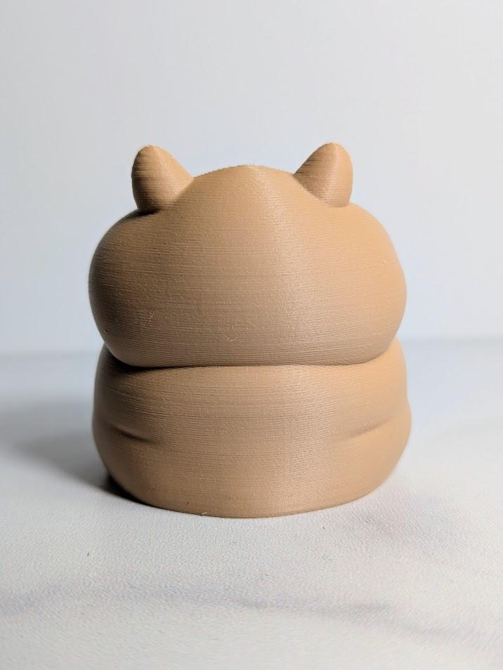 Rear view of a plump hamster figurine with small ears and a rounded back.