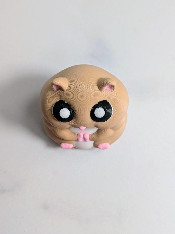 Front view of a round hamster figurine with big eyes and tiny pink feet