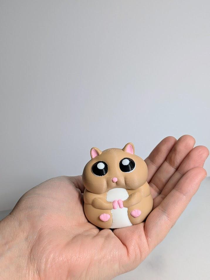 Small hamster figurine resting in an open hand, showing its compact size and round shape.