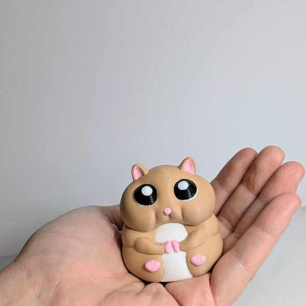 Small hamster figurine resting in an open hand, showing its compact size and round shape.