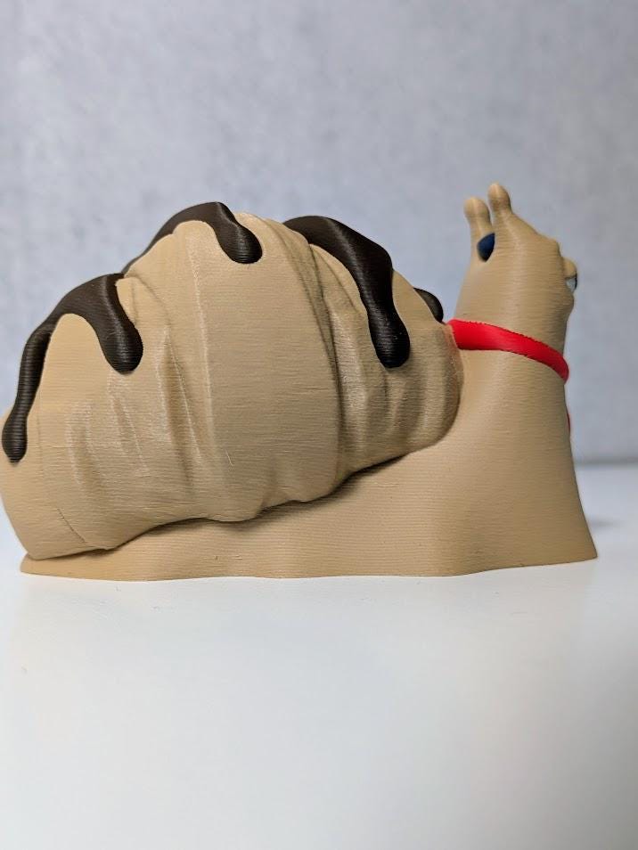 Le Escargôutier™, a croissant snail with a mustache and red neckerchief, gazes smugly to the side with his flaky shell coiled behind him.