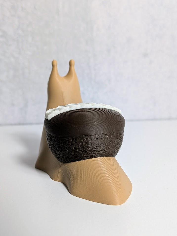 Rear view of a cupcake snail showing off its chocolate cupcake shell with white frosting peeking over the edge.