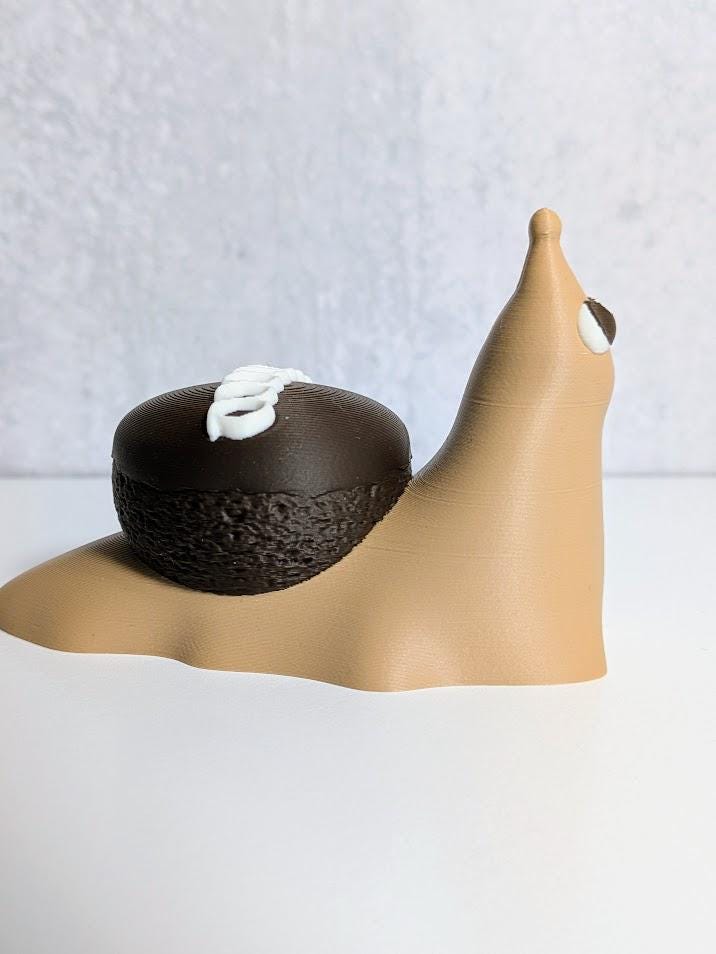 Side view of a cupcake snail figurine with a tan body and a chocolate cupcake for a shell, topped with white frosting