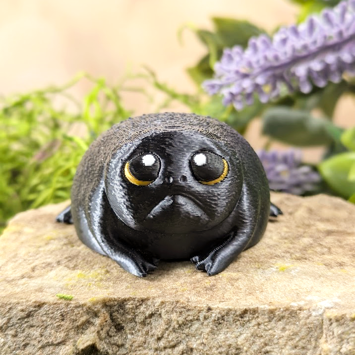 Front-facing image of the frog figurine, highlighting its large sorrowful eyes, pouty mouth, and glossy finish.