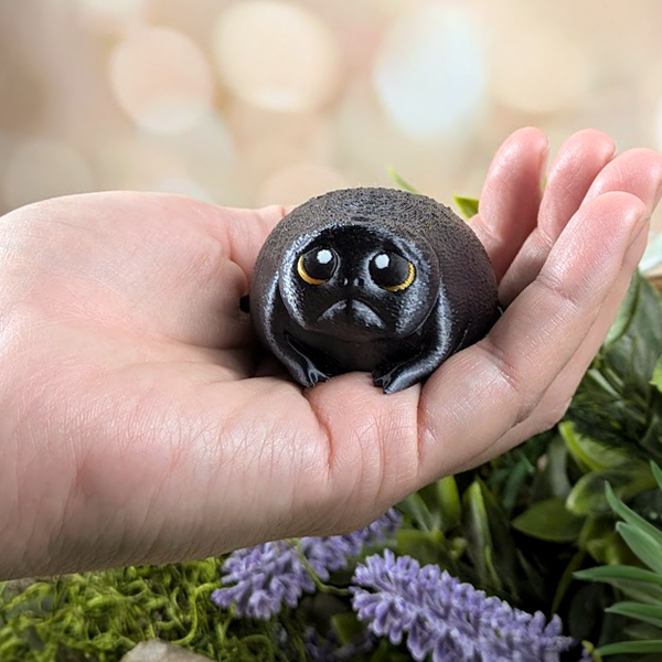 Depressed Dumpling frog resting in a human hand, showing scale and the tiny, chubby form with dramatic golden eyes.