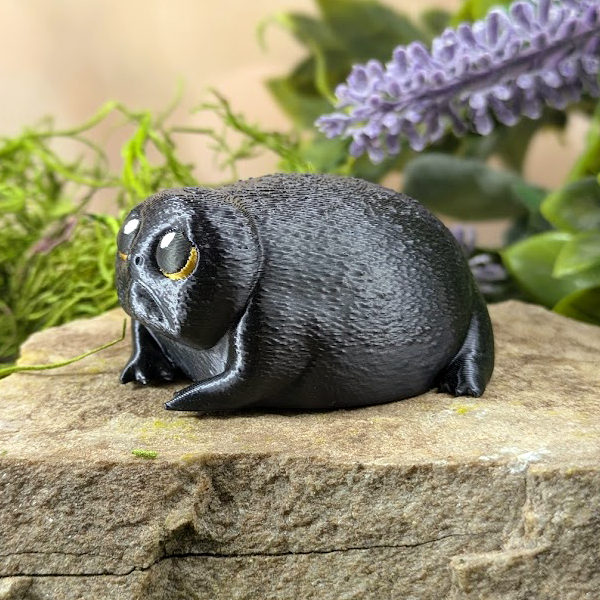 Left profile of the figurine, emphasizing the frog's plump shape and forlorn expression with a purple floral background.