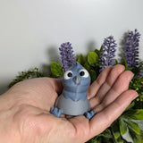 A single derpy pigeon figurine perched in an open hand, surrounded by lavender and lush foliage, ready to forget why he walked into the room.