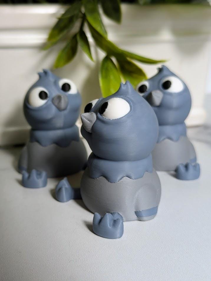 Side view of a derpy pigeon figurine showing off their huge eyes and tiny wings beneath hanging greenery.