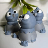 Side view of a derpy pigeon figurine showing off their huge eyes and tiny wings beneath hanging greenery.