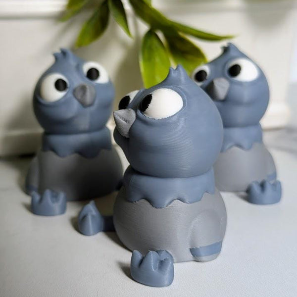 Side view of a derpy pigeon figurine showing off their huge eyes and tiny wings beneath hanging greenery.