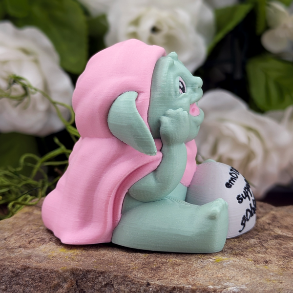 Right side profile of the goblin figurine smiling with its hand under its chin. The stone in front of it reads “emotional support goblin.”